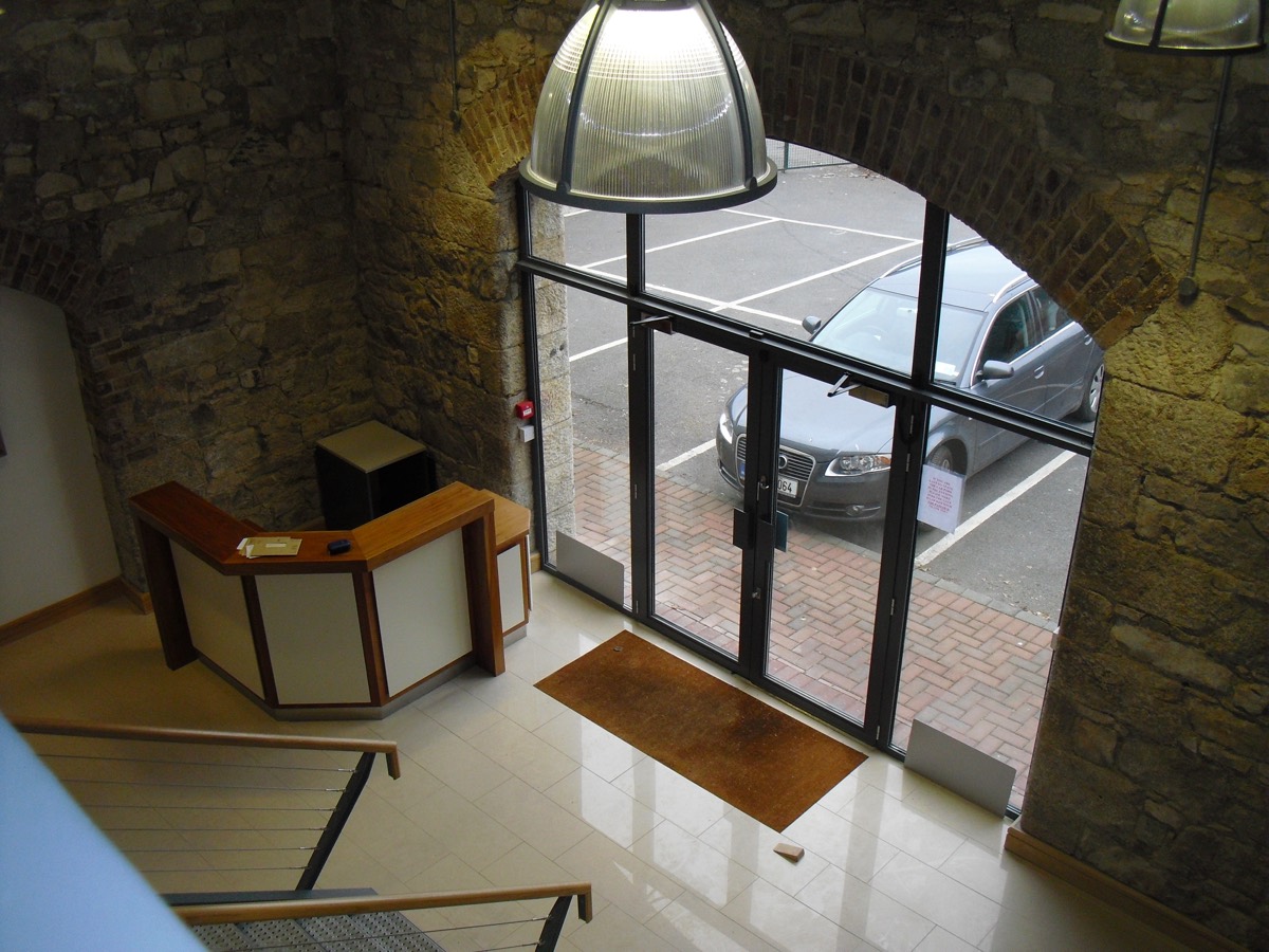 Looking down the steel stair into the double-height reception: granite walls, a brick arch and the glazed entrance